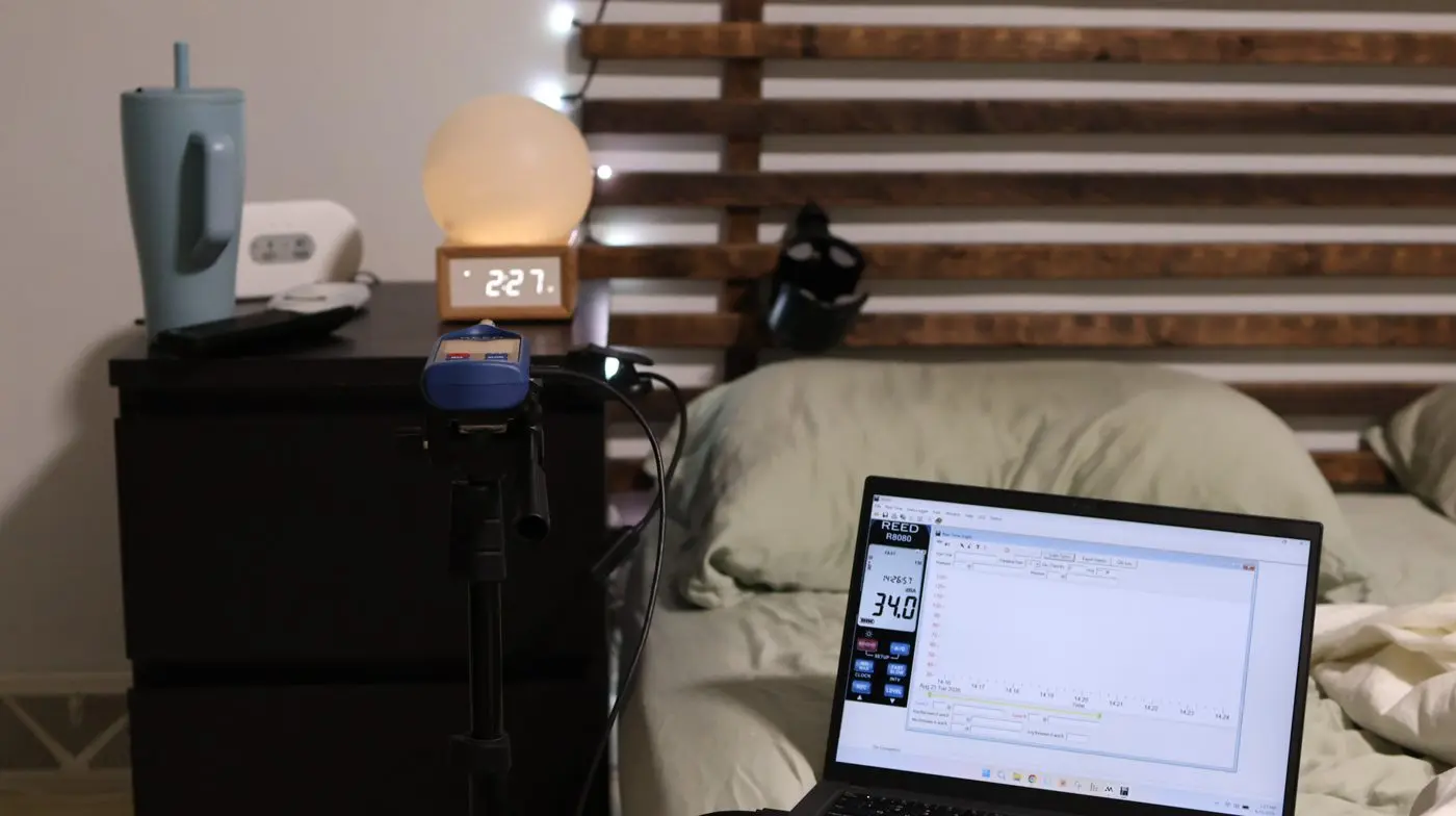 A bedside sound-level test with a laptop logging decibels next to a sunrise clock