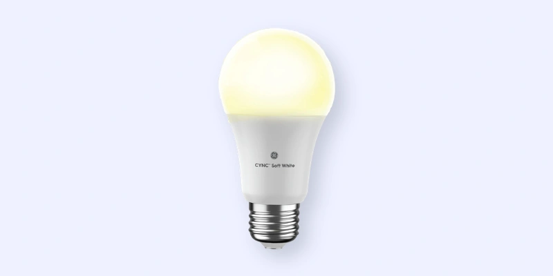 A single white LED light bulb glowing softly against a light gray background. The bulb has a standard screw base and a rounded top, with Cync Soft White printed on its side.