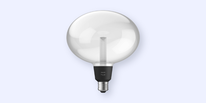 A large, round, clear glass Philips Hue smart light bulb with a visible inner filament and a silver screw base, set against a light gray background.