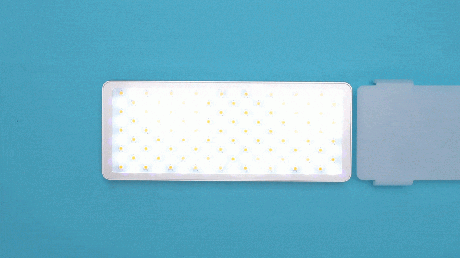 A rectangular LED panel light with multiple small yellow bulbs is illuminated against a solid blue background.