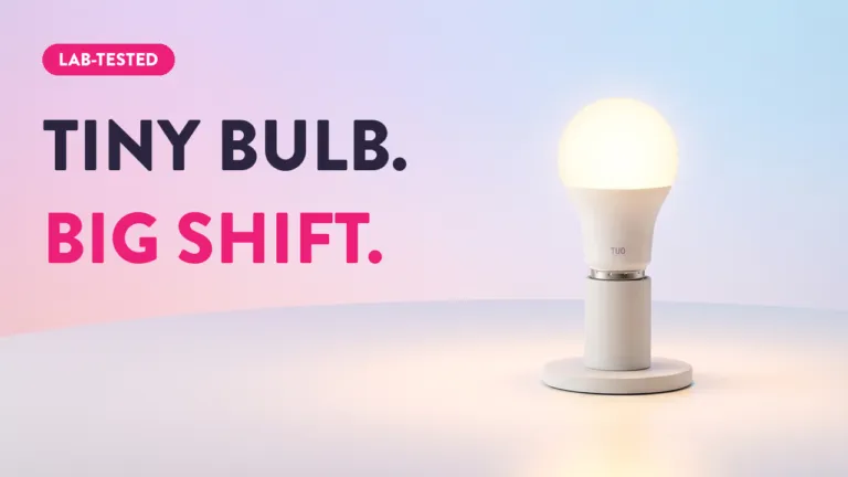 TUO smart LED bulb glowing warm white on display stand with "Tiny Bulb. Big Shift." lab-tested tagline