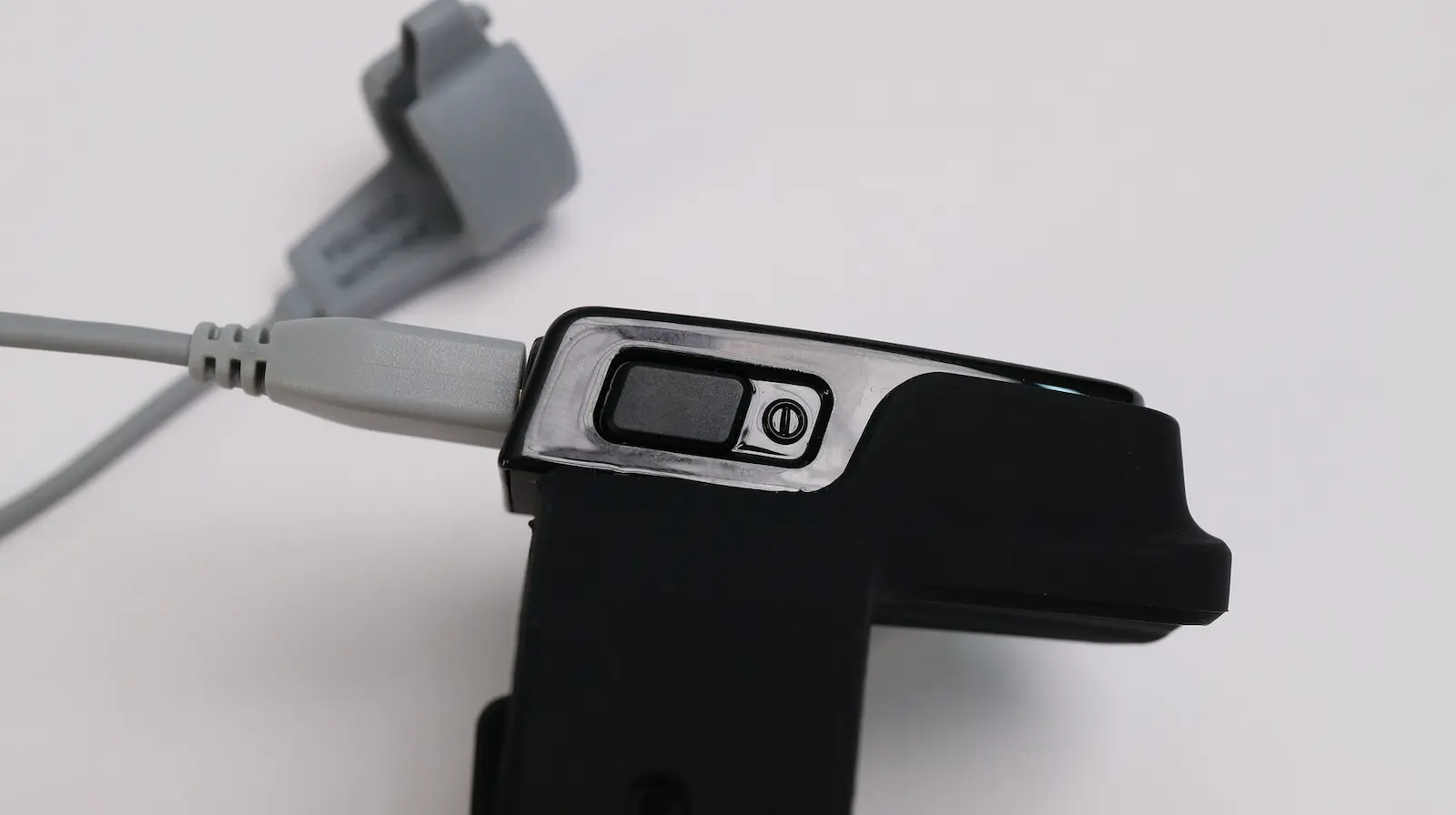 Close-up of a black plastic game controller handle with a gray cord attached. There is a rectangular button and a circular symbol next to it on the top side of the controller. The background is plain white.