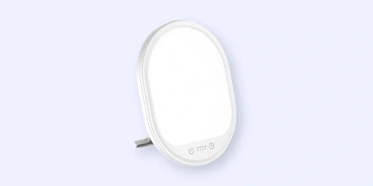 A small, oval-shaped light therapy lamp with a stand and touch controls at the bottom, set against a light blue background.