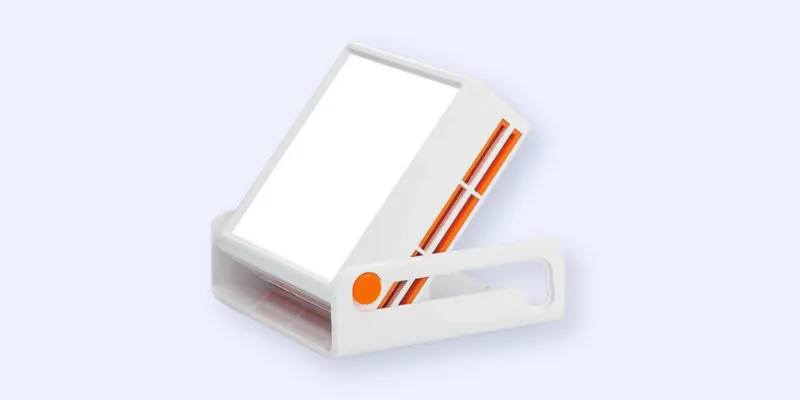 A white rectangular light therapy lamp with orange accents sits on a matching white stand against a light background. The lamp is angled upward, and its front panel emits a bright light.