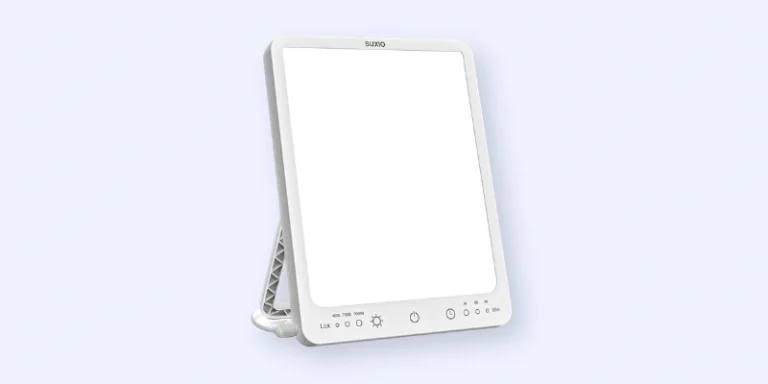 A rectangular white light therapy lamp with a stand, featuring control buttons and indicator lights along the bottom edge, against a light blue background.