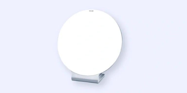 A round, white tabletop mirror with a simple, modern stand, set against a light blue background.