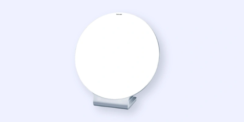 A round, white tabletop mirror with a simple, modern stand, set against a light blue background.
