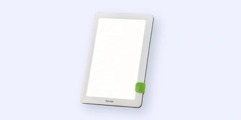 A rectangular light therapy lamp with a white frame, a green clip on one side, and the brand name beurer at the bottom, set against a light blue background.