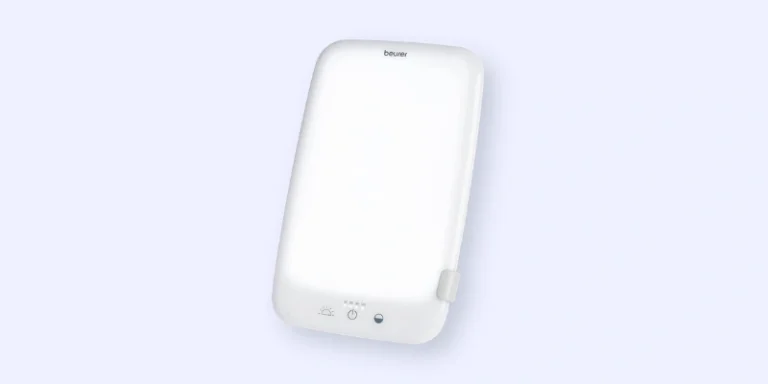 A rectangular white light therapy lamp with a minimalist design, featuring a small button and indicator lights at the bottom front panel, against a light blue background.