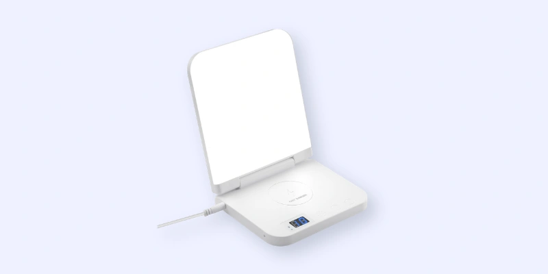A white, rectangular device with a hinged, illuminated mirror standing upright. The base features a circular touchpad, a digital display, and a charging cable connected on the left side.