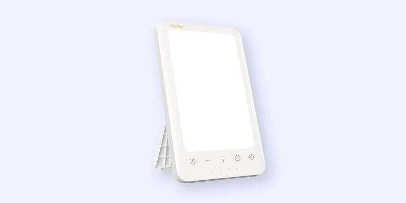 A rectangular white therapy light with touch controls and a stand, positioned at an angle against a light blue background.