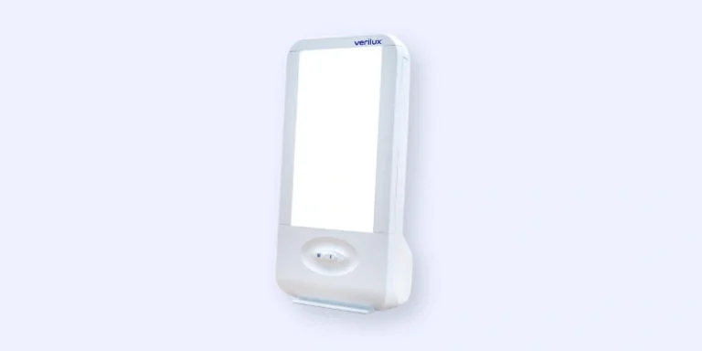 A rectangular light therapy lamp with a white frame and a glowing light panel, mounted on a pale background. The device is labeled Verilux at the top.
