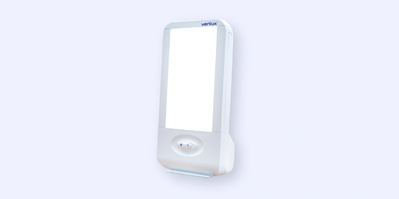A rectangular light therapy lamp with a white frame and a glowing light panel, mounted on a pale background. The device is labeled Verilux at the top.