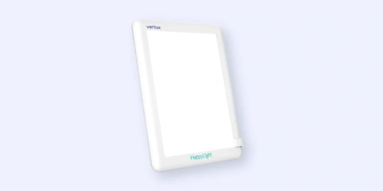 A rectangular Verilux HappyLight therapy lamp with a white frame, shown against a light blue background. The device emits bright white light and is designed for light therapy use.
