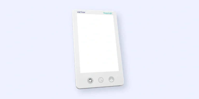 A white Verilux HappyLight therapy lamp with three round touch buttons at the bottom, glowing with a bright light on a light background.