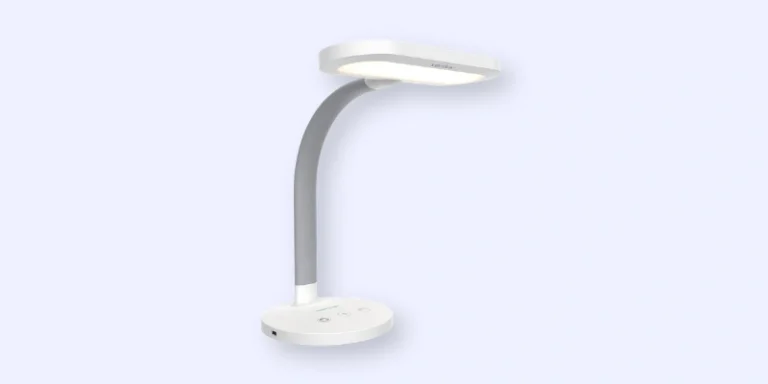 A modern, white desk lamp with a curved gray neck and a flat, oval-shaped light head, shown against a light blue background. The base has touch controls and a power port.