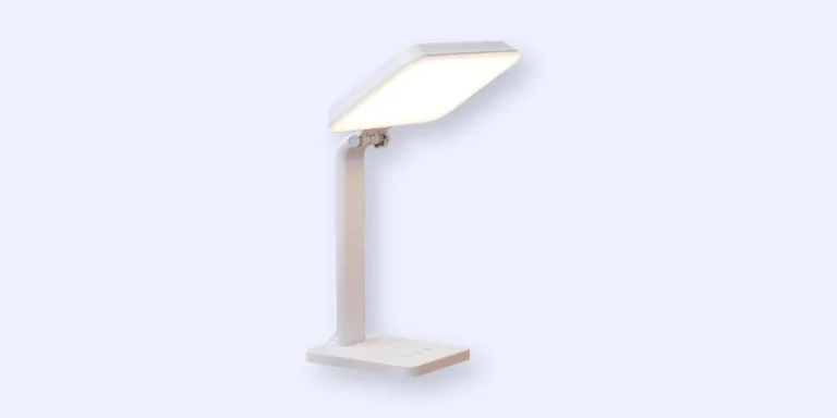 A modern, minimalist white desk lamp with a rectangular LED light panel, angled downward, and a sturdy base, set against a light blue background.