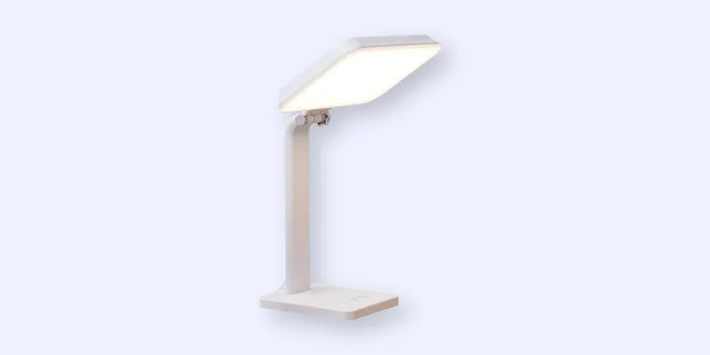 A modern, minimalist white desk lamp with a rectangular LED light panel, angled downward, and a sturdy base, set against a light blue background.