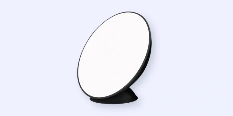 A white, circular satellite dish with a black rim and base, angled to the left, set against a light blue background.