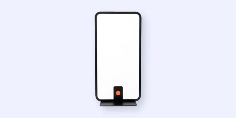 A rectangular, black-framed whiteboard stands upright on a flat base, featuring a small orange circle at the bottom center against a light background.