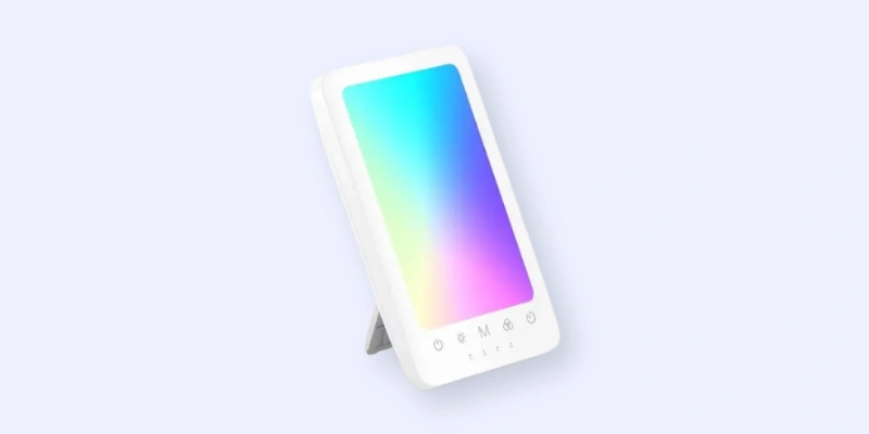A rectangular LED light therapy lamp with a white frame and stand, displaying a gradient of blue, purple, pink, and green light on its screen, set against a light background.