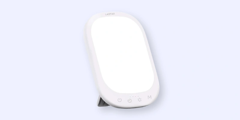 A rectangular white light therapy lamp with rounded edges, a stand at the back, and touch control buttons at the bottom on a light blue background.