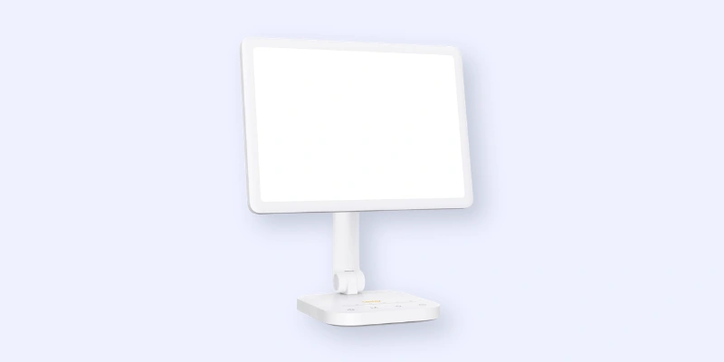 A white touchscreen monitor with a wide, blank display is mounted on a slim, adjustable stand attached to a rectangular base against a light blue background.