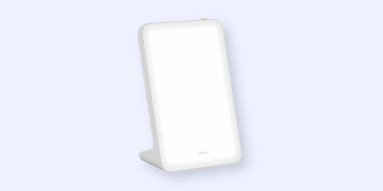 A rectangular white light therapy lamp with rounded edges, standing upright on a flat base against a light blue background.