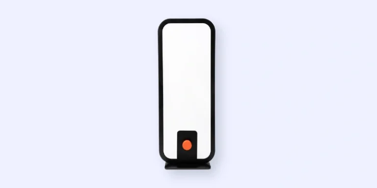 A rectangular, upright electronic device with a black frame, white front panel, and a small orange circle near the bottom, set against a light background.
