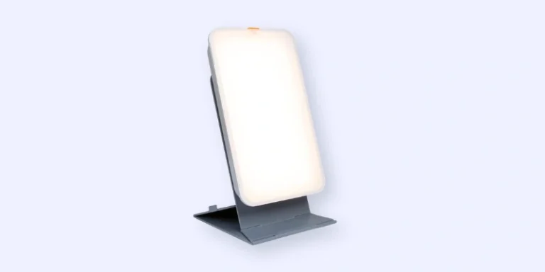 A rectangular light therapy lamp with a white glowing screen, positioned upright on a gray adjustable stand against a light background.