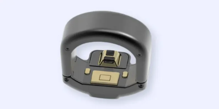 A close-up of a black and gold electronic device with a curved handle and exposed circuit components, viewed from above against a light gray background.