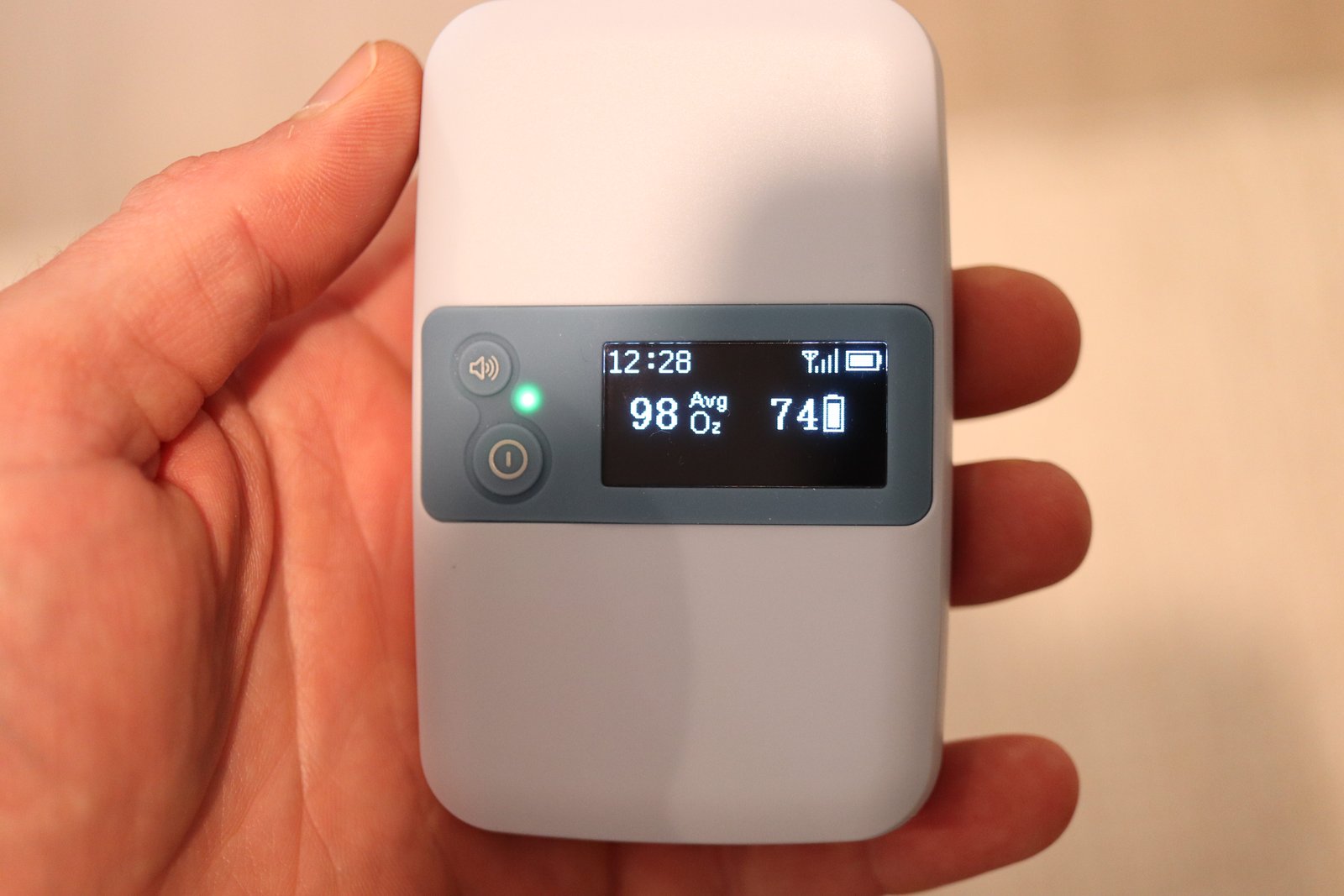 Hand holding a portable pulse oximeter displaying 98% average SpO2 oxygen saturation and heart rate of 74 BPM