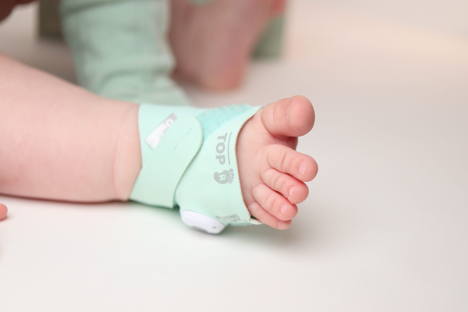 Newborn baby foot with mint green hospital monitoring band showing TOP R label
