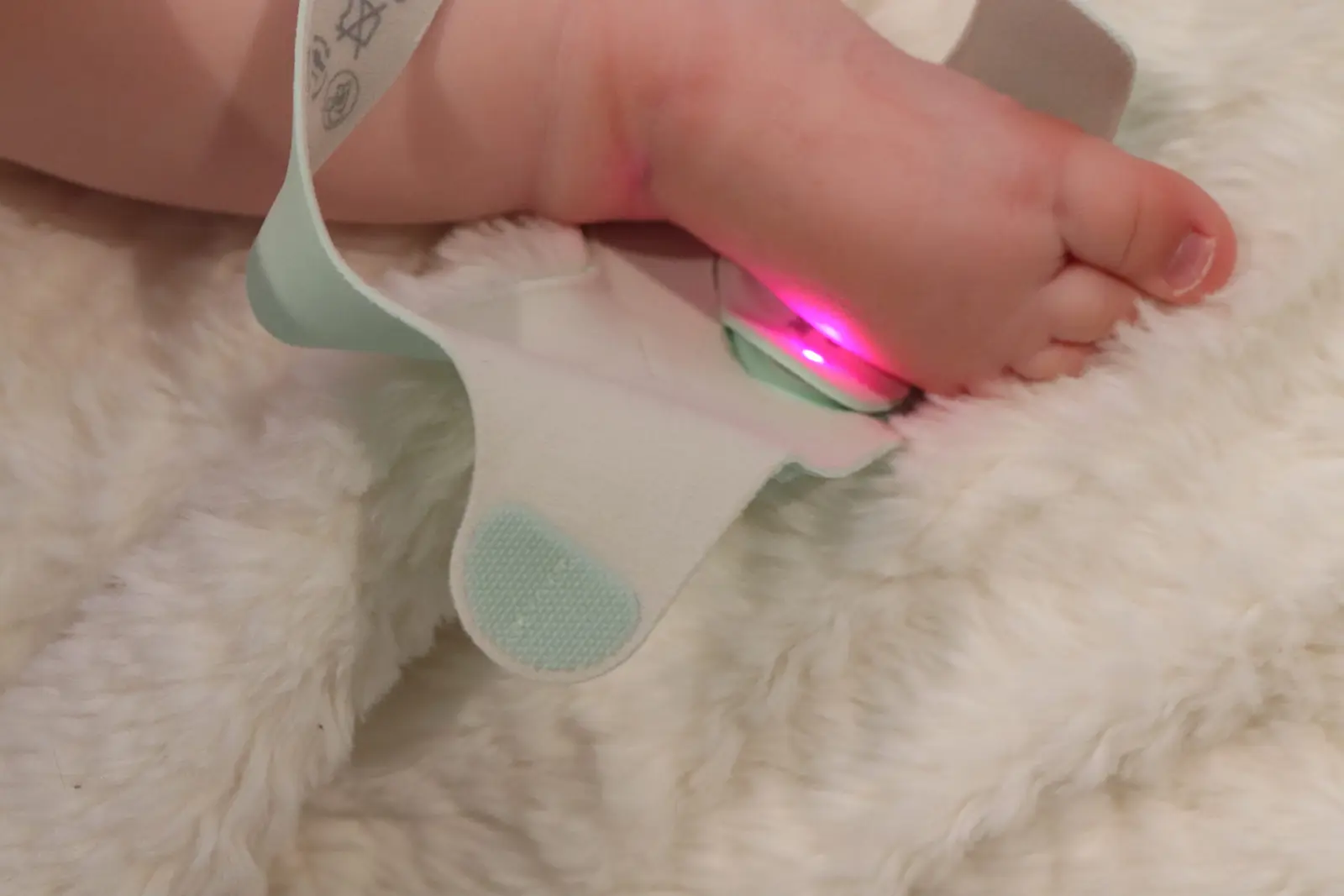 Pulse oximeter sensor with red light on newborn baby foot measuring oxygen saturation
