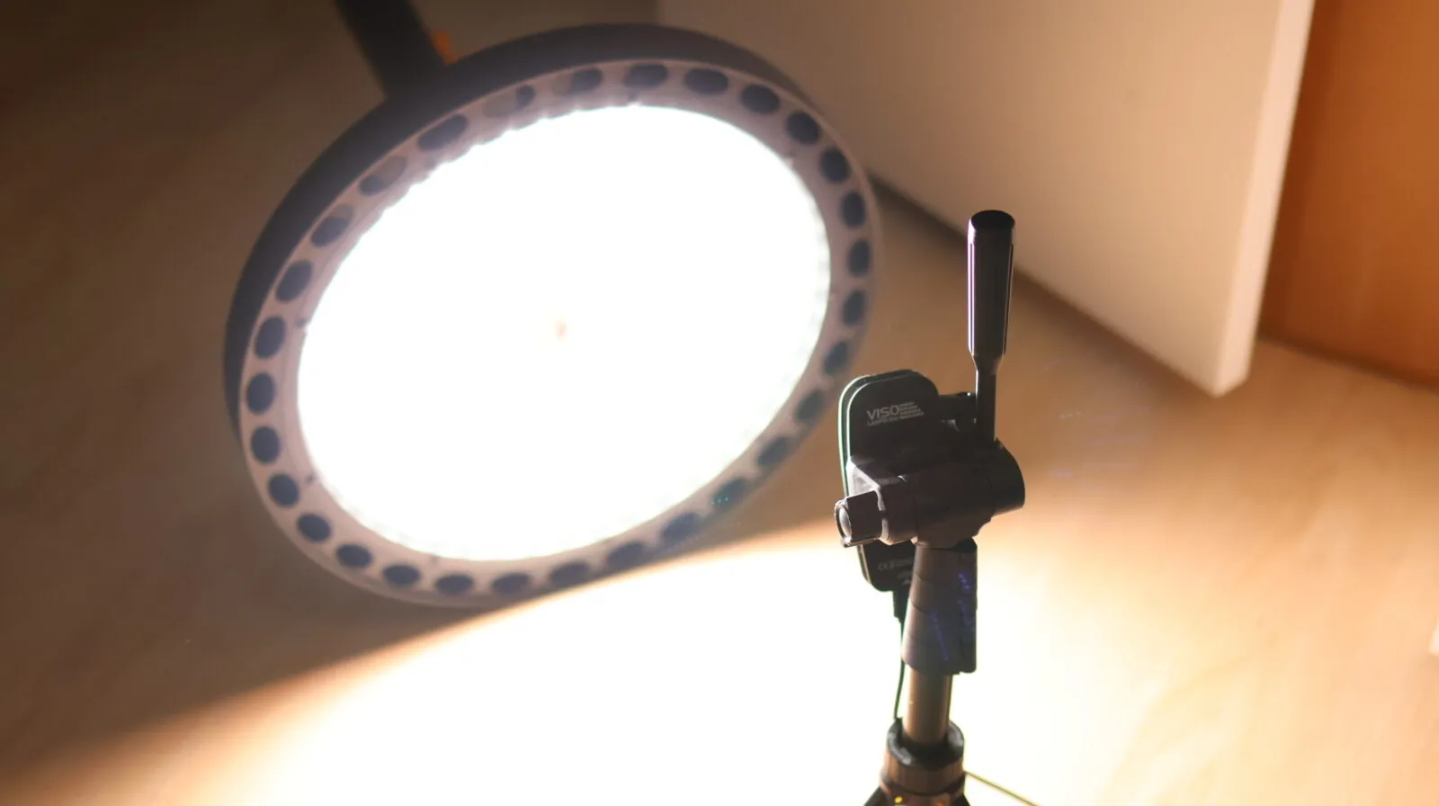Bright LED ring light on a tripod stand illuminating a studio setup with warm background glow