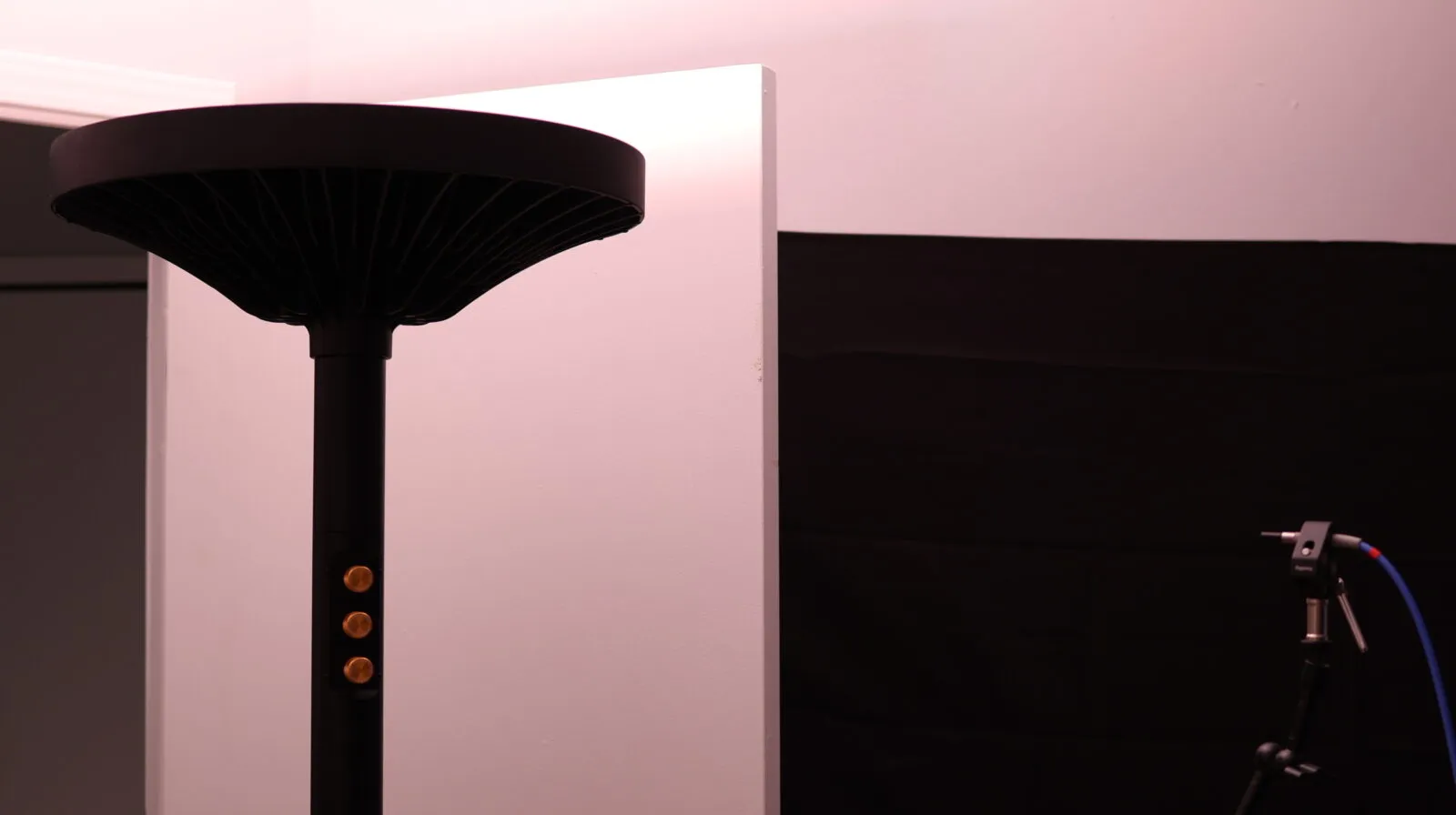 Black floor lamp with mushroom-shaped diffuser and brass knobs beside white panel in dark studio