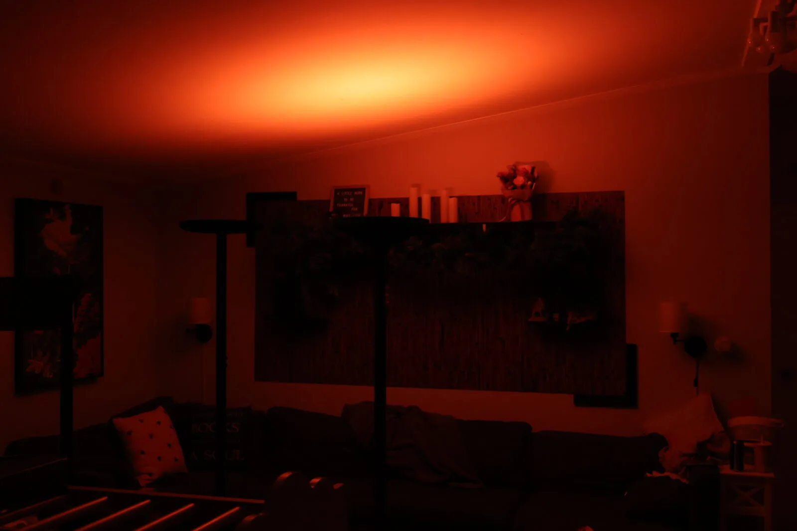 Bedroom bathed in warm red ambient lighting from an LED lamp, illuminating shelves with candles and decor above a dark sofa