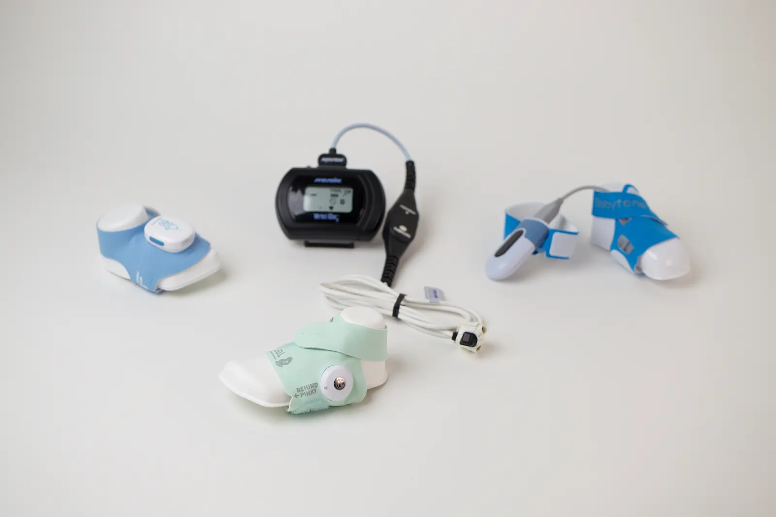 Collection of wearable TENS therapy devices including Bluetens, Mytone, and Avalanche units with cables on white surface