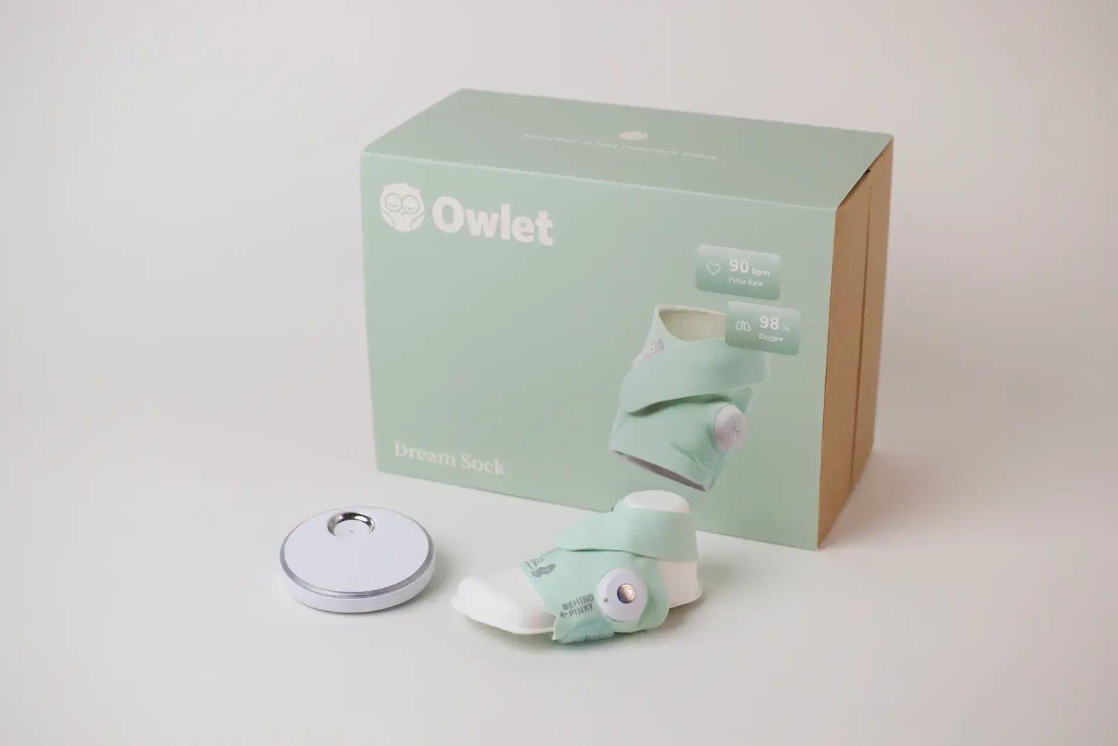 Owlet Dream Sock baby monitor with mint sock, sensor pod, and base station beside product packaging box