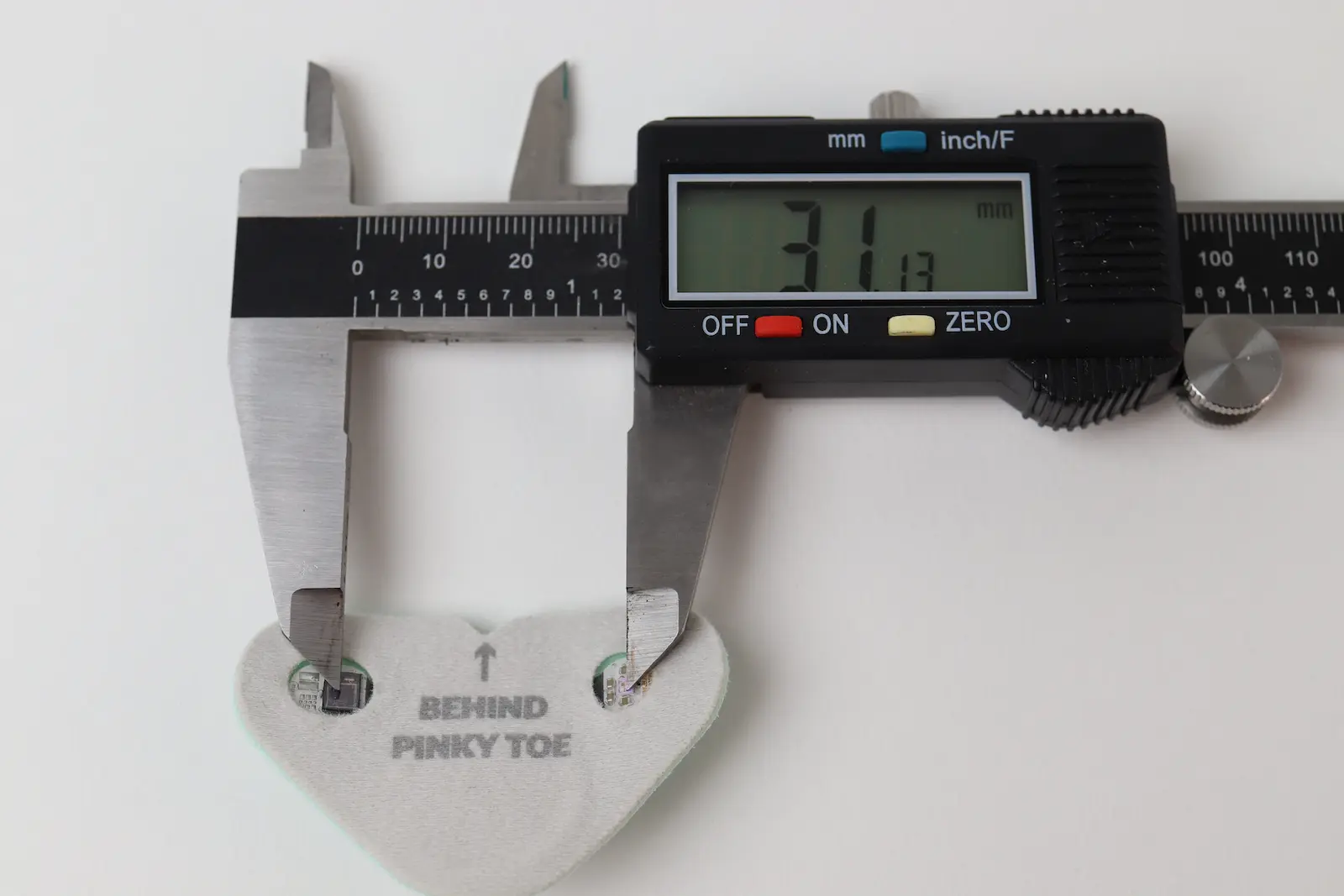 Digital calipers measuring a foam foot pad labeled Behind Pinky Toe, displaying 31.13mm width on LCD screen