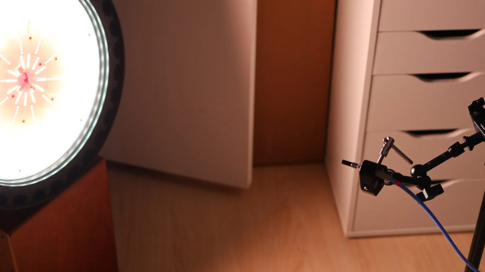 LED ring light illuminating a home studio setup with acoustic panels, drawer unit, and microphone arm with blue cable