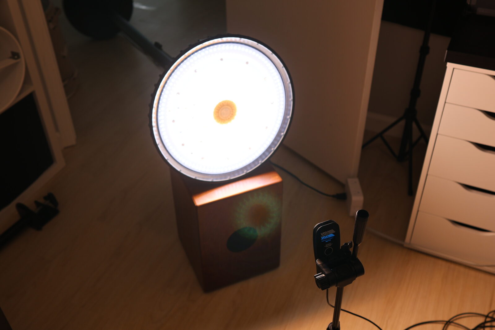 Large circular LED ring light on wooden base in home studio setup with camera trigger on tripod stand