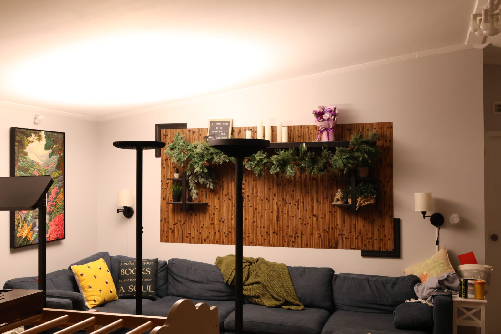 Cozy living room with blue sectional sofa, bamboo wood accent wall, greenery garland, candles, and decorative shelves