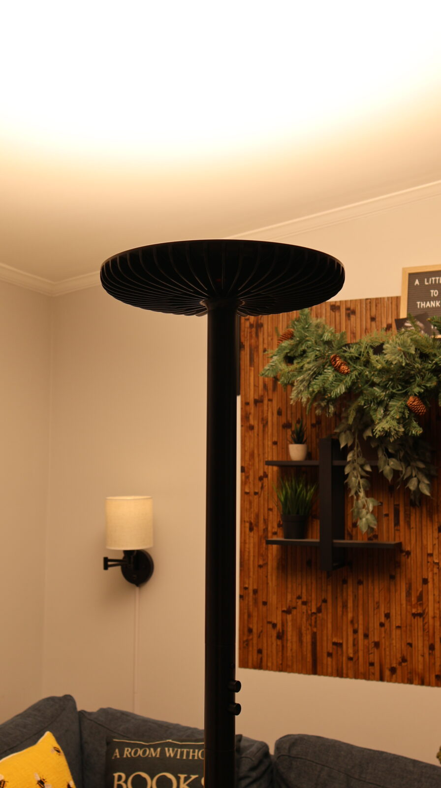 Black torchiere floor lamp with decorative mushroom shade illuminating a cozy living room with wooden wall panel and holiday