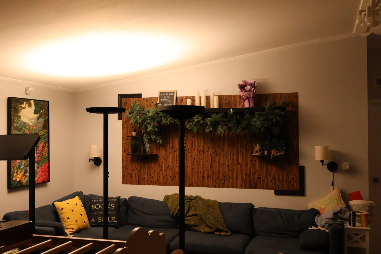 Cozy living room with blue sectional sofa, bamboo accent wall, holiday garland, candles, and warm floor lamp lighting