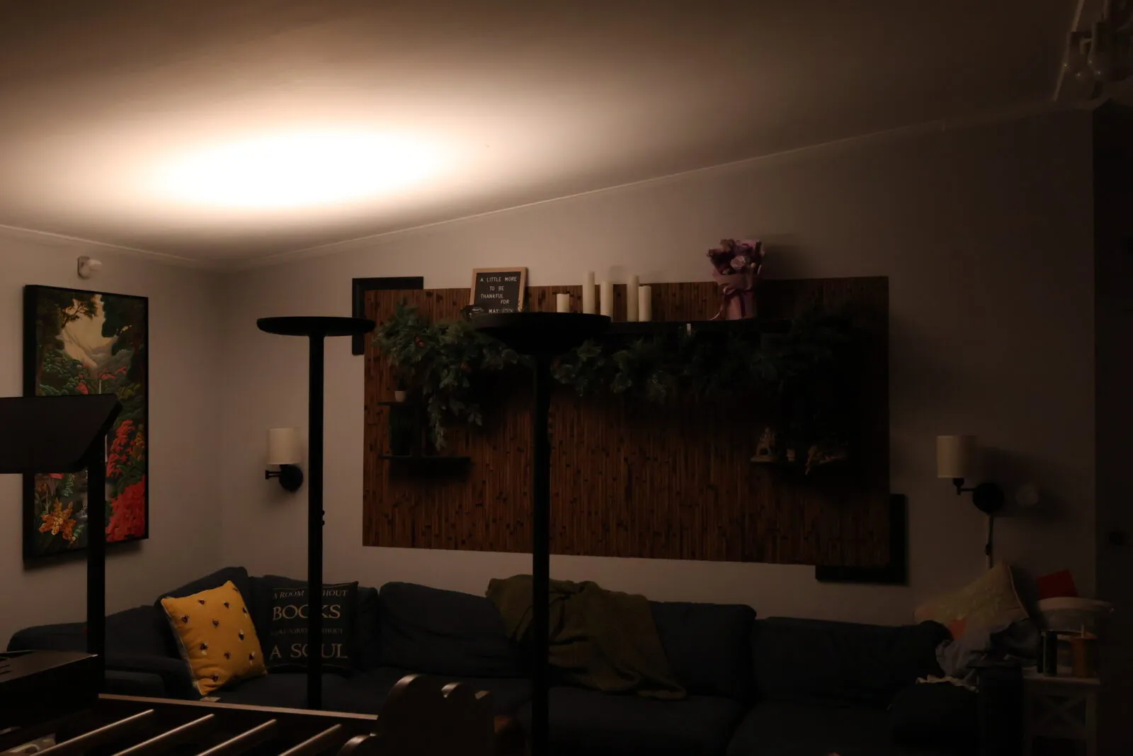 Cozy living room with warm floor lamp lighting, dark sofa with decorative pillows, wooden wall shelves with greenery and cand