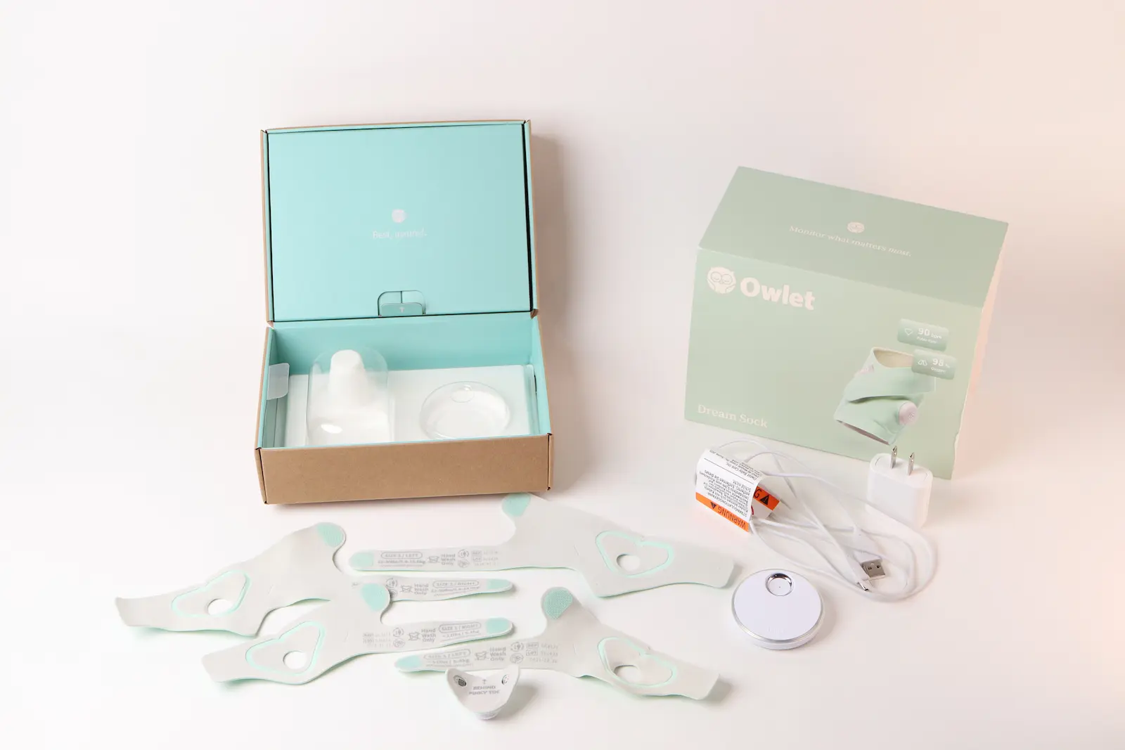 Owlet Dream Sock baby monitor unboxed, showing sensor, fabric socks, base station, charging cable, and mint packaging