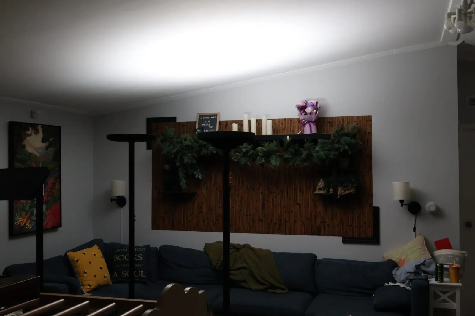 Cozy living room with navy blue sectional sofa, wooden accent wall, holiday garland, candles, and floral bouquet