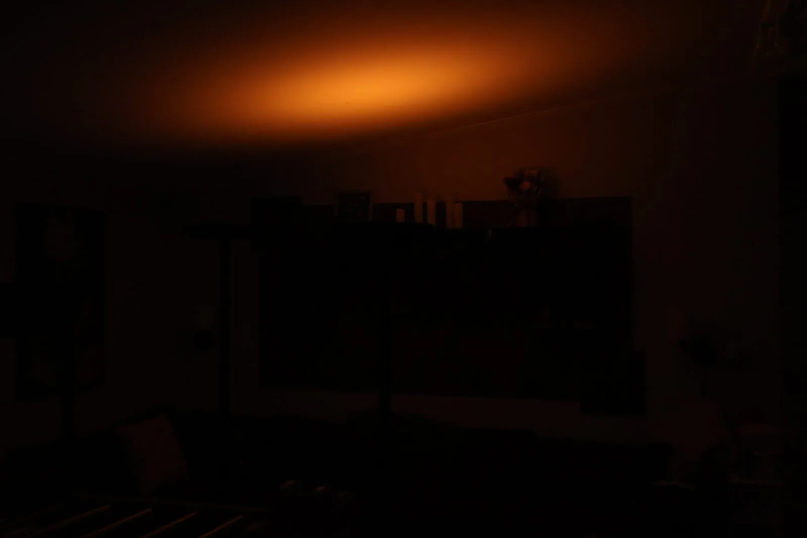 Dimly lit room bathed in warm orange ambient light glowing on ceiling above dark furniture