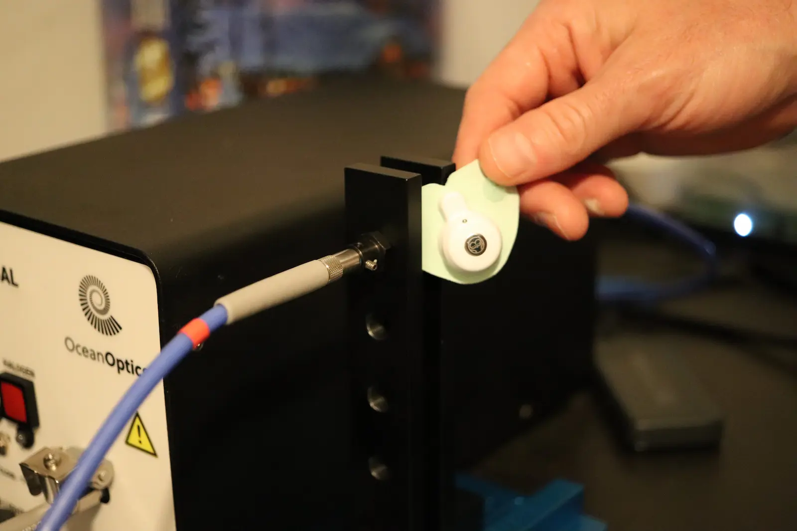 Hand inserting fiber optic connector into Ocean Optics spectrometer port with blue optical fiber cable attached